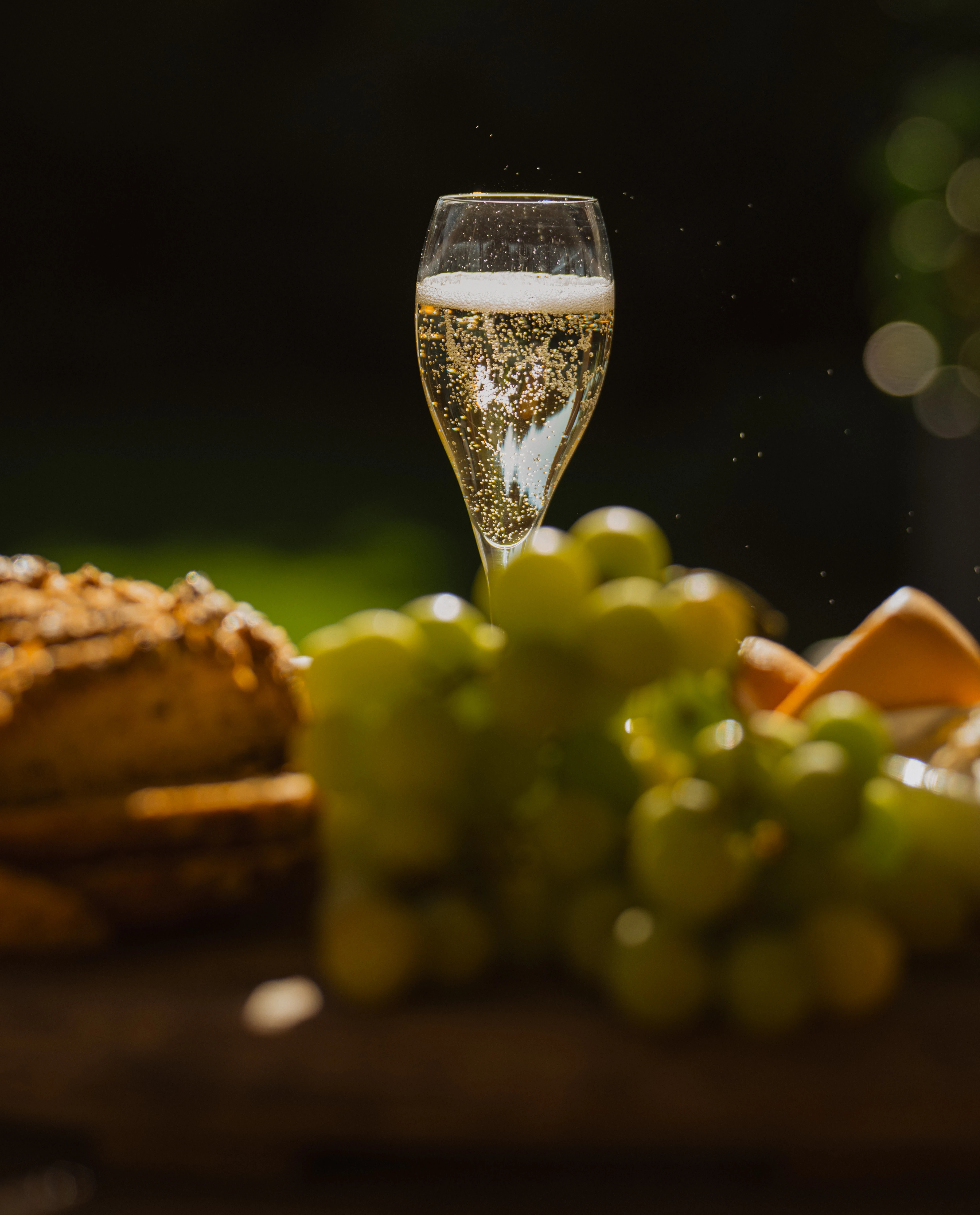 A glass of Cap Classique beside bread and grapes at an outdoor table